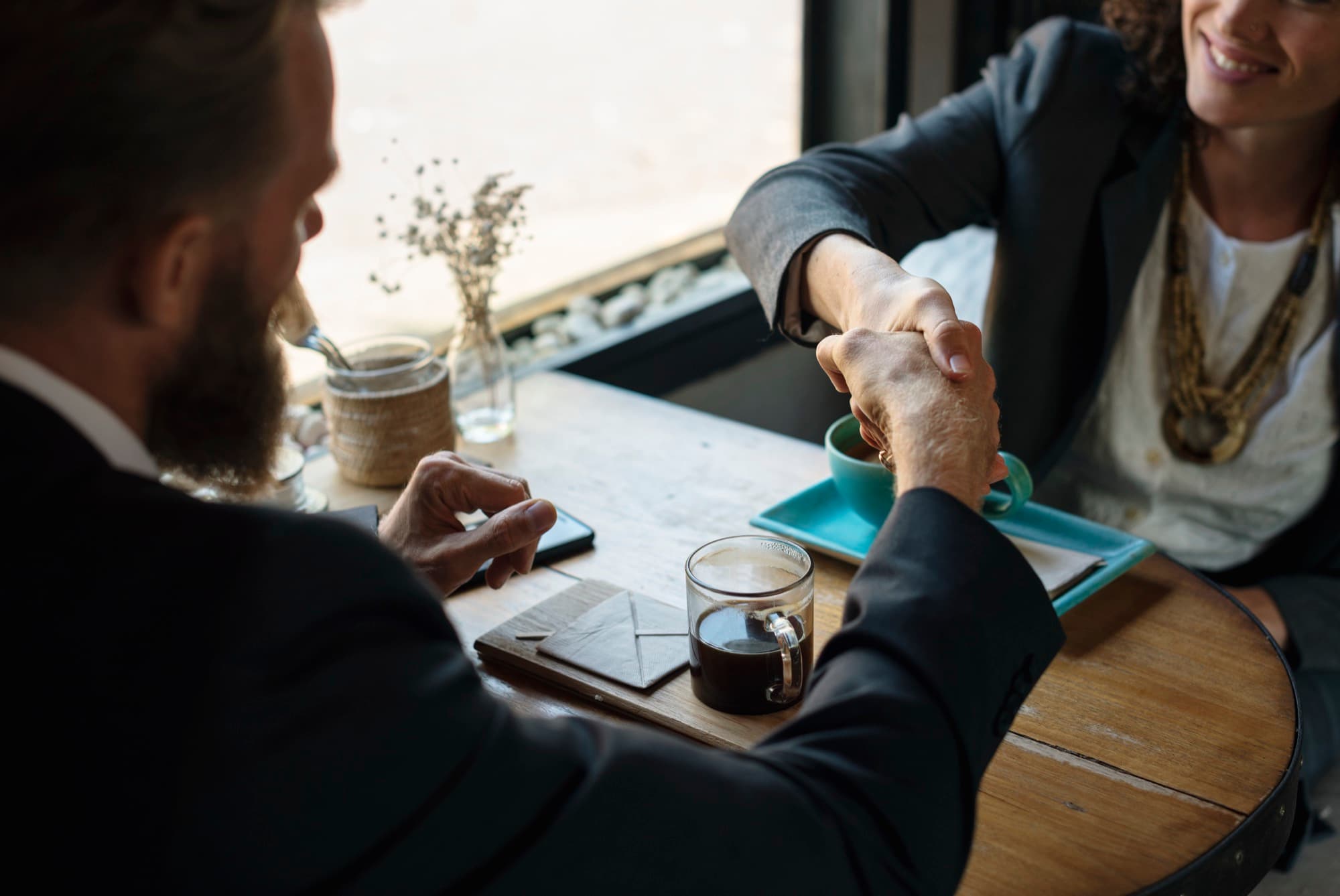 Two business partners shaking hands over a coffee shop table